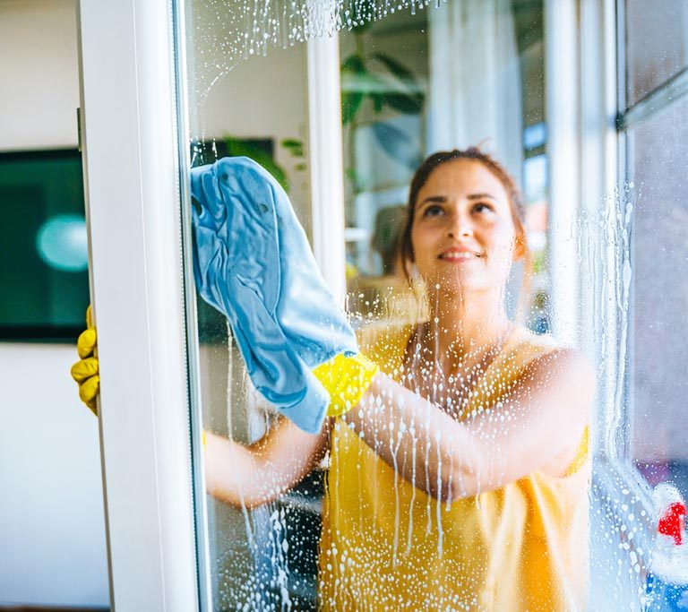 Beautiful smiling young woman cleaning and wiping window with spray bottle and rag stock photo